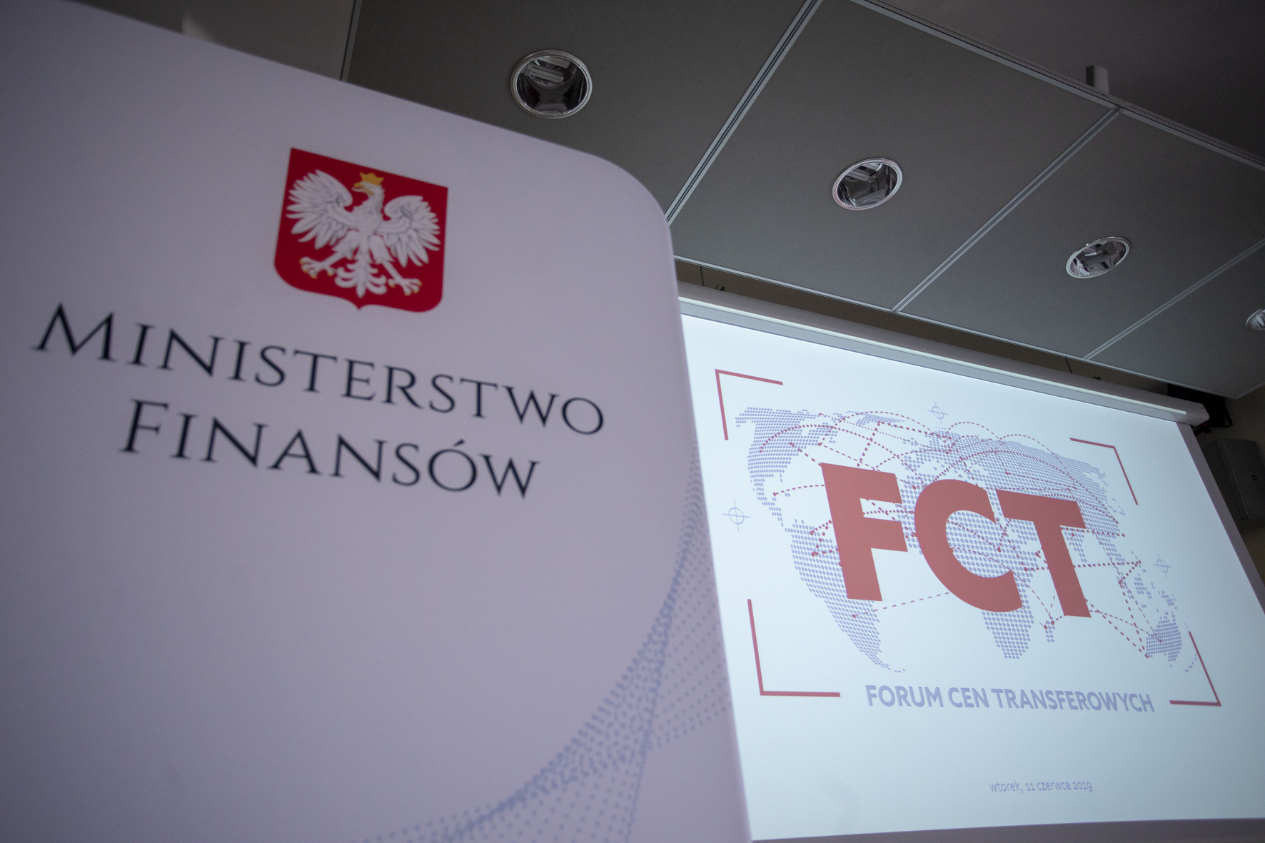 Biały baner z godłem Polski i napisem Ministerstwo Finansów. W tle ekran prezentacji. Czerwony napis FCT na szarym zarysie mapy świata. Pod nim szary napis Forum Cen Transferowych.